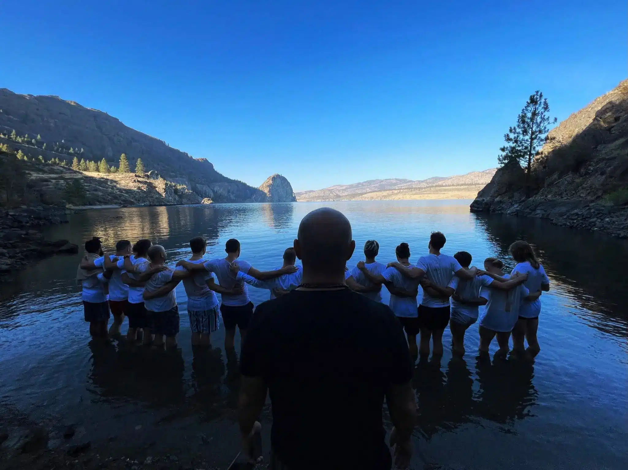 Amir facing the men of the Men's Work Intensive, arms linked, standing in the water at sunset