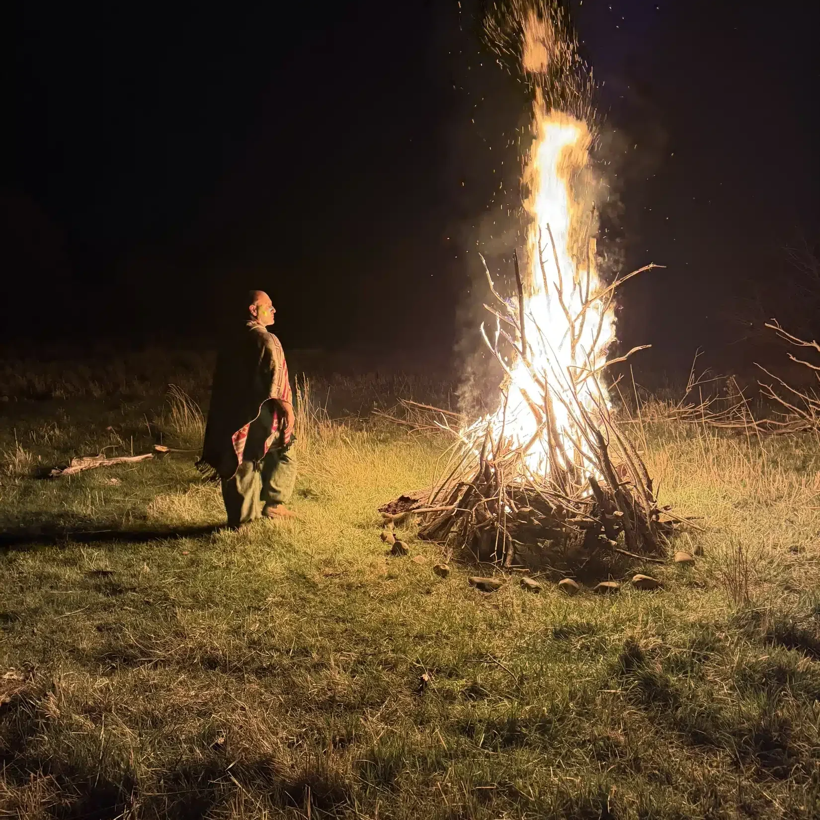 A shaman-robed figure stands before a bonfire at night